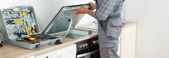 Cooktop repair technician lifting a built-in stovetop for service in Houston, TX