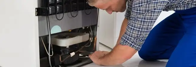 Refrigerator repair technician servicing the compressor and condenser area in Houston, TX