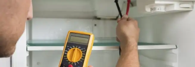 Refrigerator repair technician testing electrical components with a multimeter in Houston, TX
